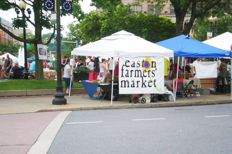 A vibrant scene at the Farmers Market in Easton, showcasing colorful stalls filled with fresh produce, flowers, and handmade goods, bustling with activity. Unmissable Places to Visit in Pennsylvania